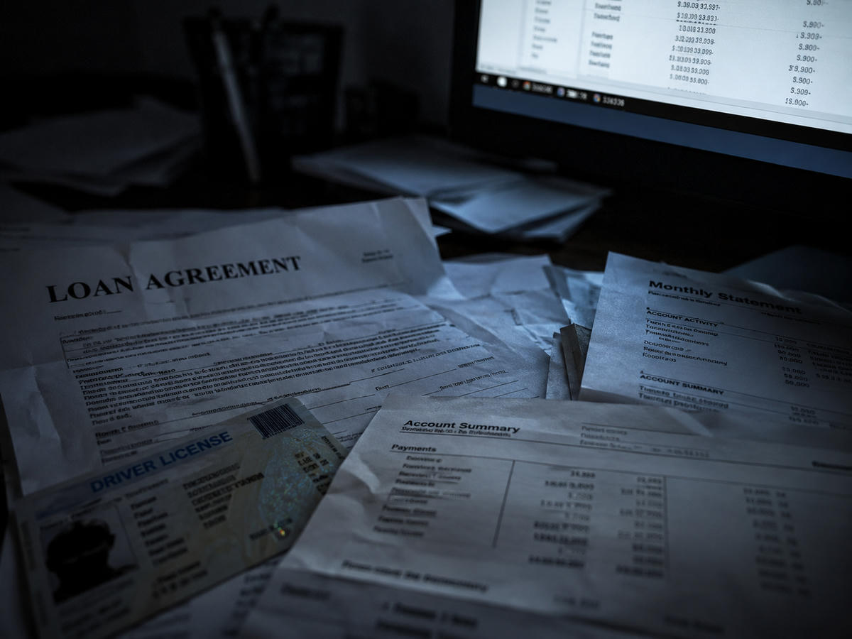 Contrats de prêt, un permis de conduire et des relevés financiers éparpillés sur un bureau sous la lumière froide d'un écran, illustrant le type de documents sensibles exposés lors de la faille Heights Finance.